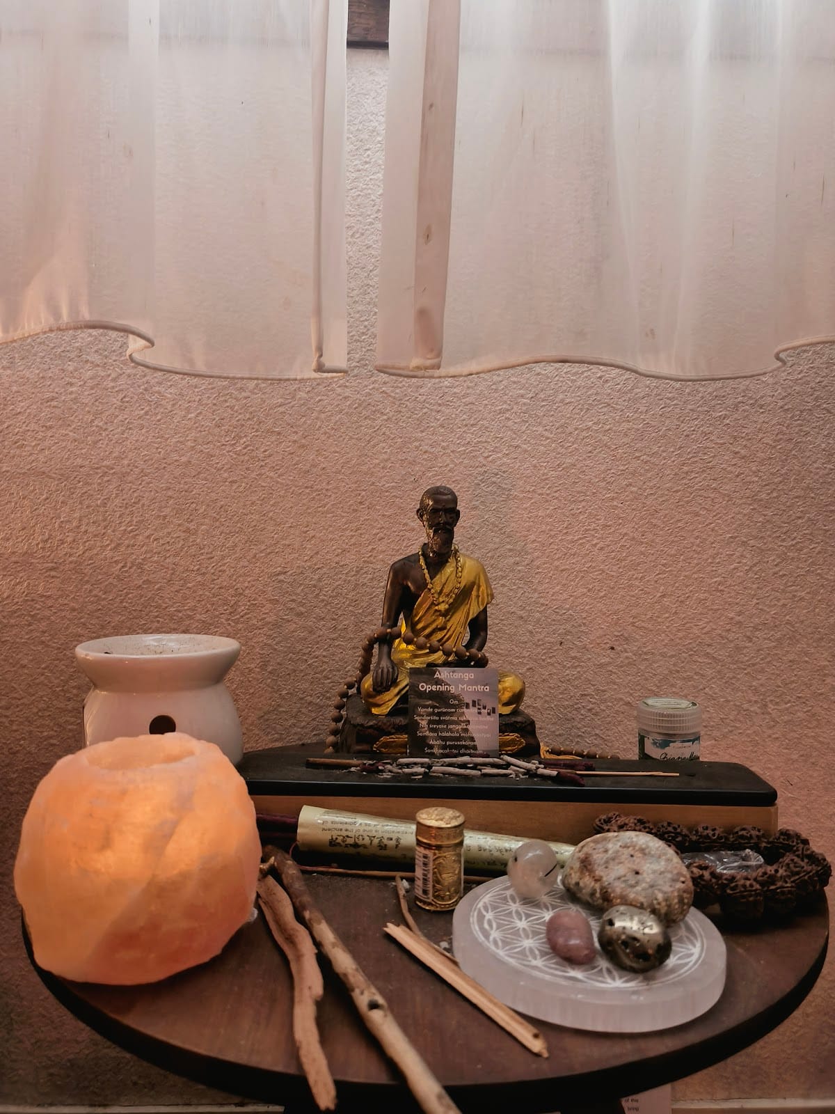 L'autel de la salle : une lampe de sel allumée, une statuette dorée, de l'encens, des pierres et des cristaux sur une petite table ronde en bois.